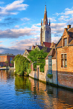 Bruges Belgium vintage stone houses and bridge over canal ancient medieval street picturesque landscape in summery sunny day with blue sky white clouds.