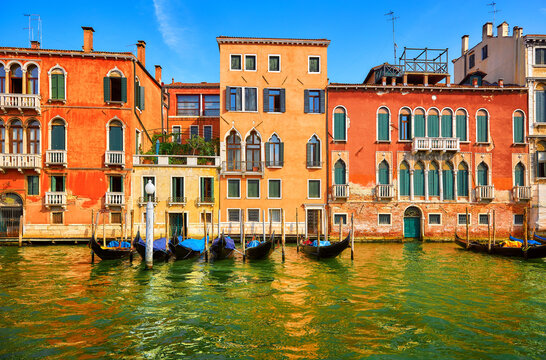 Venice, Italy. Gondolas with floating at piers by Grand Canal among antique buildings and traditional italian Venetian architecture. Sunny evening sunset with blue sky and clouds.