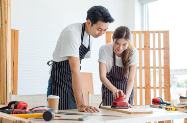Asian professional male carpenter in apron complimenting showing thumb up to female lover worker...