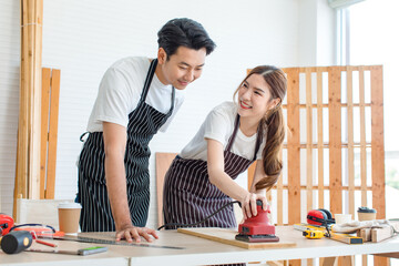 Asian professional male carpenter in apron complimenting showing thumb up to female lover worker...