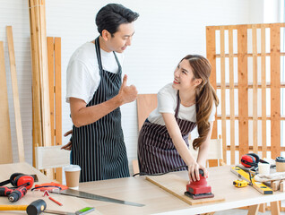 Asian professional male carpenter in apron complimenting showing thumb up to female lover worker...