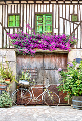 Fototapeta na wymiar Medieval village in Europe - Wooden framed house facade with flowers on the balconies and old bicycle with flowers.