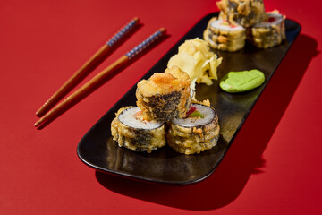Lavish close-up tempura sushi roll with avocado, eel, and tobiko on a black plate; the red background with hard shadows makes it a standout for Asian menu
