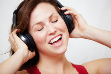 Fototapeta premium Music, headphones and singing by happy woman in studio with audio, track or song on white background. Earphones, face and female person streaming podcast, radio or online playlist and subscription