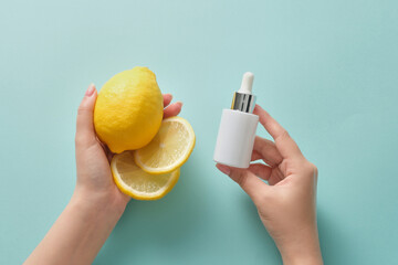 Top view of female hand is holding a fresh lemon and lemon slices, the other hand is holding white dropper bottle unbranded mockup. Cosmetics concept with natural extract rich in vitamin C