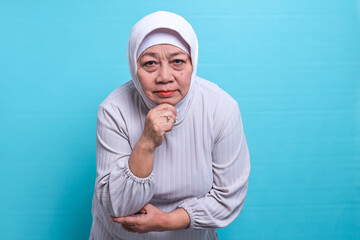 I am watching you. Happy elderly Asian muslim woman wearing hijab posing confident with smiling and looking at camera isolated on blue background