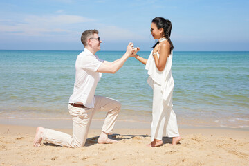 young man showing engagement ring and surprise his girlfriend on the beach