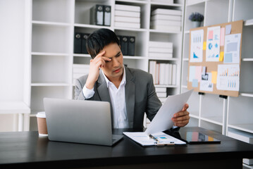 Asian business man is stressed, bored, and overthinking from working on a tablet at the modern...