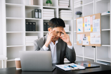 Asian business man is stressed, bored, and overthinking from working on a tablet at the modern office.
