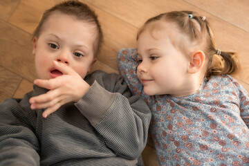 Boy plays with his younger sister on the bed in home bedroom. Down syndrome and ASD