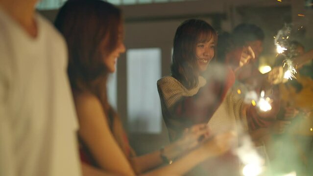Group of Happy young Asian man and woman friends enjoy and fun outdoor activity celebration meeting party playing sparklers firework together at home backyard on summer holiday vacation at night.