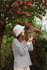 Side view portrait of beautiful woman standing near branching spring tree. wearing striped shirt and panama smelling enjoying blossoming and beautiful nature.