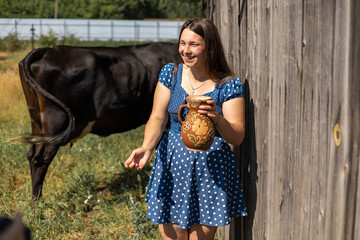 Young farmer woman smiling on camera carries jug of milk after milking cow on farm pasture. Natural...