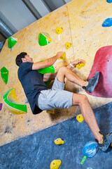 One Professional Male Rock climber man hanging on a bouldering climbing wall, inside on colored hooks.