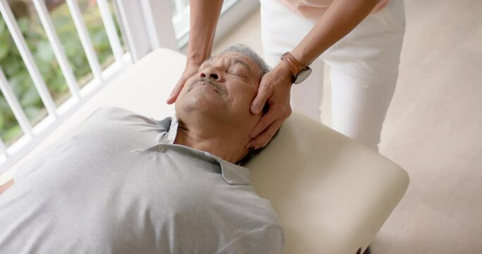 Diverse male physiotherapist advising and senior male patient exercising on couch, in slow motion