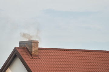 Dark smoke comes out of the chimney of a modern house in winter. Heating with solid fuel. The concept of environmental pollution