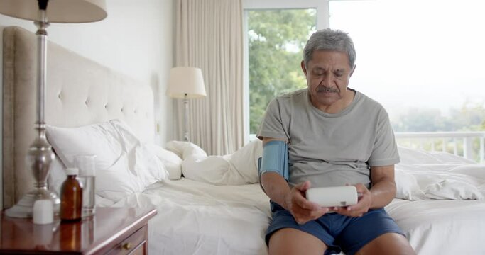 Biracial senior man testing blood pressure in bed at home, slow motion