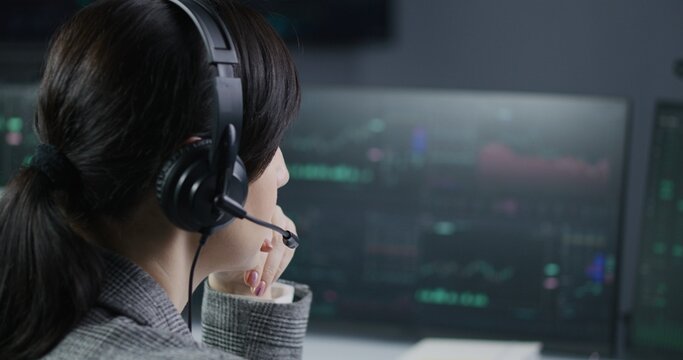 Close up of female financial analyst in headset working in broker agency office. Businesswoman looks at computer screen, monitors real-time stocks, exchange market charts. Cryptocurrency trading. - Powered by Adobe