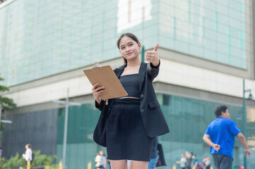 A lovely lady standing outside, in the city wearing a black suit, and black skirt holding up a...