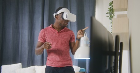 African American man emotional talks and gesticulates on online conference using VR headset. Gamer...