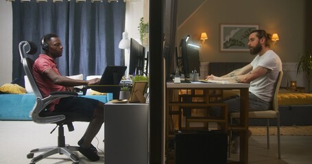 Two diverse neighbors sit at computers. One man starts working remotely, another man in headphones...