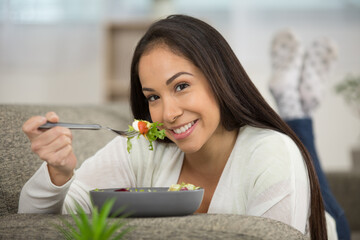 happy woman eating healthy salad on sofa at home