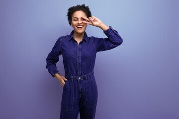 young cheerful positive brunette latin woman with afro hair gathered in a ponytail dressed in a blue stylish denim suit posing against the backdrop of copy space