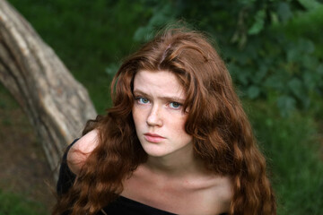 Naklejka premium Portrait of upset girl with long red hair and freckles in summer park. Offended, fright and sad mood