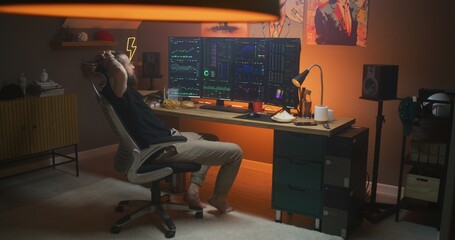Male stock trader sits on chair in front of multi-monitor computer with real-time stocks, exchange market charts. Man works remotely in cryptocurrency trading at home office. Investment, analytics.