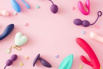 Adult erotic toys concept. Top view arrangement of vibrators, anal plugs, vaginal balls, colorful hearts on pastel pink background with empty space for text or advert - obrazy, fototapety, plakaty