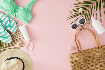 The idea of a summer beach getaway. Top view photo of stylish bag, hat, eyewear, swimsuit, flip flops, cosmetic bottles, palm leaves and seashell on pink background with space for advert or text