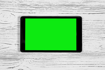 Black tablet with green screen on a wooden table mock up. Copy space chroma key display.