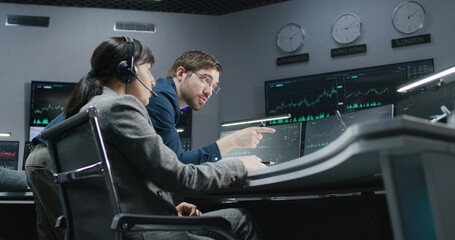 Financial analysts monitor and discuss real-time stocks data on computer. Businesspeople work in bank office. Big digital screens with exchange market charts. Cryptocurrency trading and analytics.
