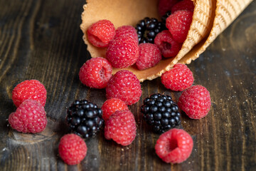 Red ripe raspberries with waffle cups on a black table