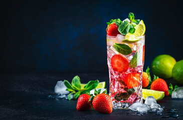 Summer strawberry mojito cocktail with lime, white rum, soda, cane sugar, mint, and ice in glass on deep blue background. Cold refreshing beverage