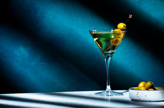 Vodka martini with olives, alcoholic cocktail drink with vodka and vermout, dark green background, bright hard light and shadow pattern, copy space