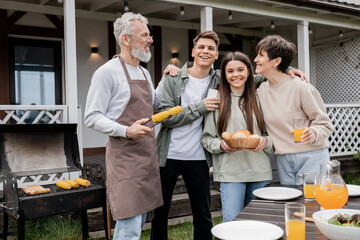 family photo, parents day, happy middle aged parents having bbq party with teenage daughter and young adult son, father holding tongs with grilled corn, summer house, suburban life