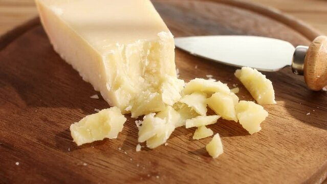 Hard cheese with a knife on a cutting board. Wooden background. Parmesan with broken pieces. Traditional Italian cheese grana parmigiano reggiano. Close-up.