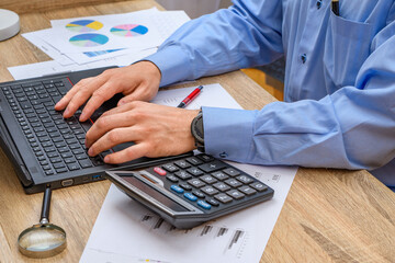 Mężczyzna przy biurku piszący przy komputerze, praca biurowa w finansach - obrazy, fototapety, plakaty