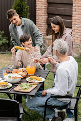 Smiling siblings standing near middle aged mother and father during family barbeque in relaxed atmosphere during parents day celebration at backyard, family love and unity concept