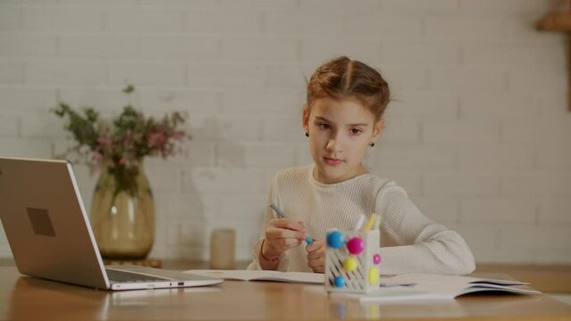 A quick-witted girl sits at her desk and is engaged in a writing lesson. Children and other learning with the help of gadgets.