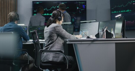 Diverse financial analysts monitor real-time stocks on computers. Team of businesspeople work in...