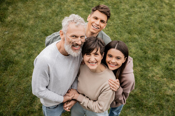 Overhead view of cheerful children hugging middle aged parents and looking at camera while celebrating parents day together at backyard in june, quality time with parents concept