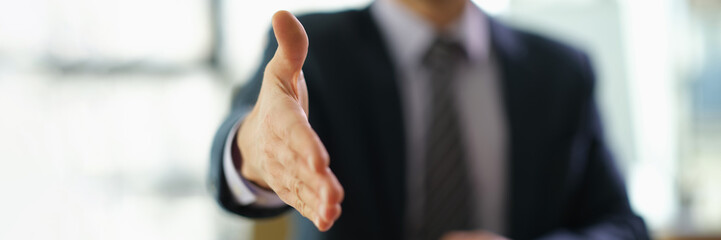 Businessman in suit extending his hand for handshake to partner at work in office closeup....