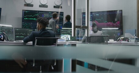 Multi ethnic team of traders work on multi-monitor computers with displayed real-time stocks....