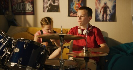 Young boy and girl play drum kit and ukulele in bedroom at night.
