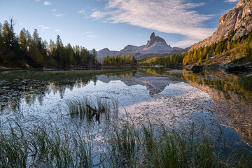 In an alpine setting, the majestic Dolomites are tinged with the warm autumn colors, while the imposing larches are colored with orange and gold, creating a reflections on the lake
