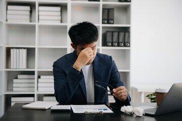 Frustrated young Asian businessman working on a laptop computer sitting at his working place in modern office