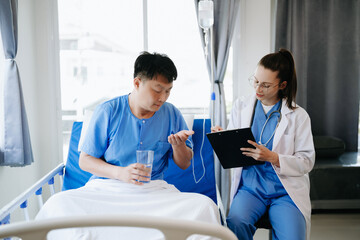 Doctor in white suit take notes while discussing and Asian elderly, man patient who lying on bed with receiving saline solution in hospital or clinic.