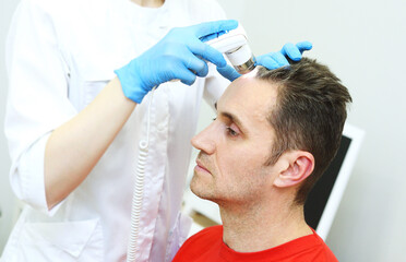 A cosmetologist-trichologist diagnoses the condition of a male patient's hair with gray hair using a trichoscope.
